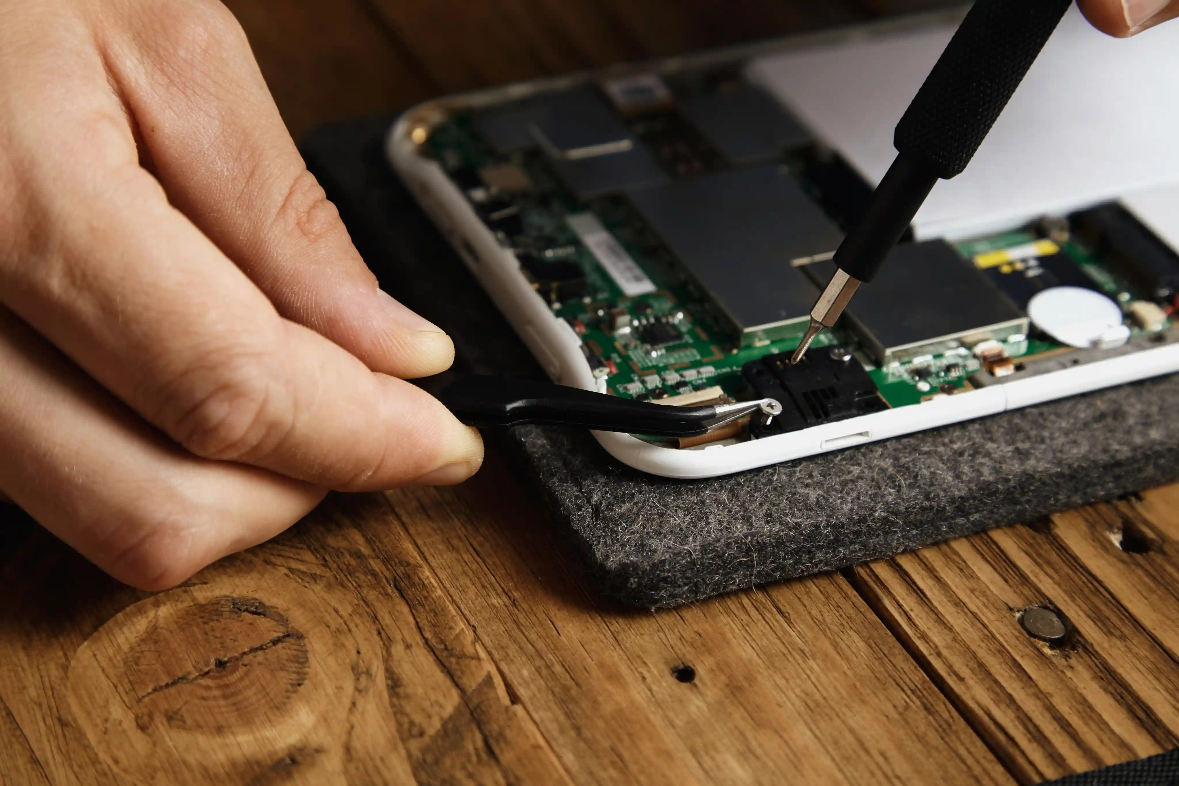 Technician repairing an open smartphone motherboard with precision tools